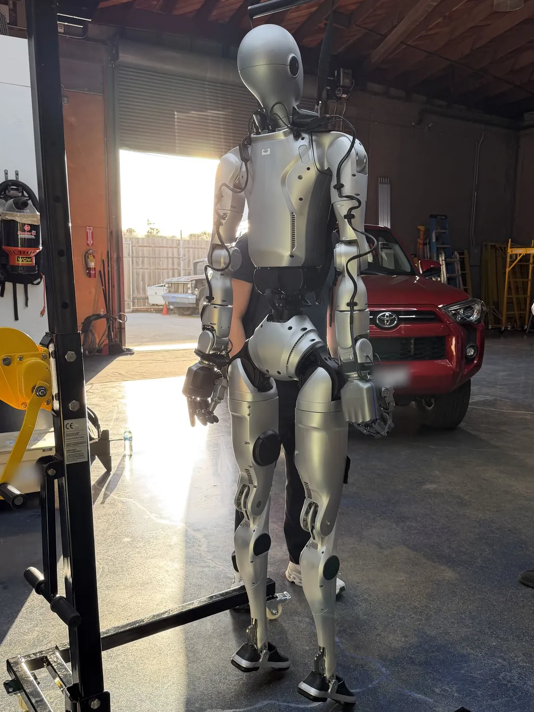 A humanoid robot hanging from a support gantry in a workshop