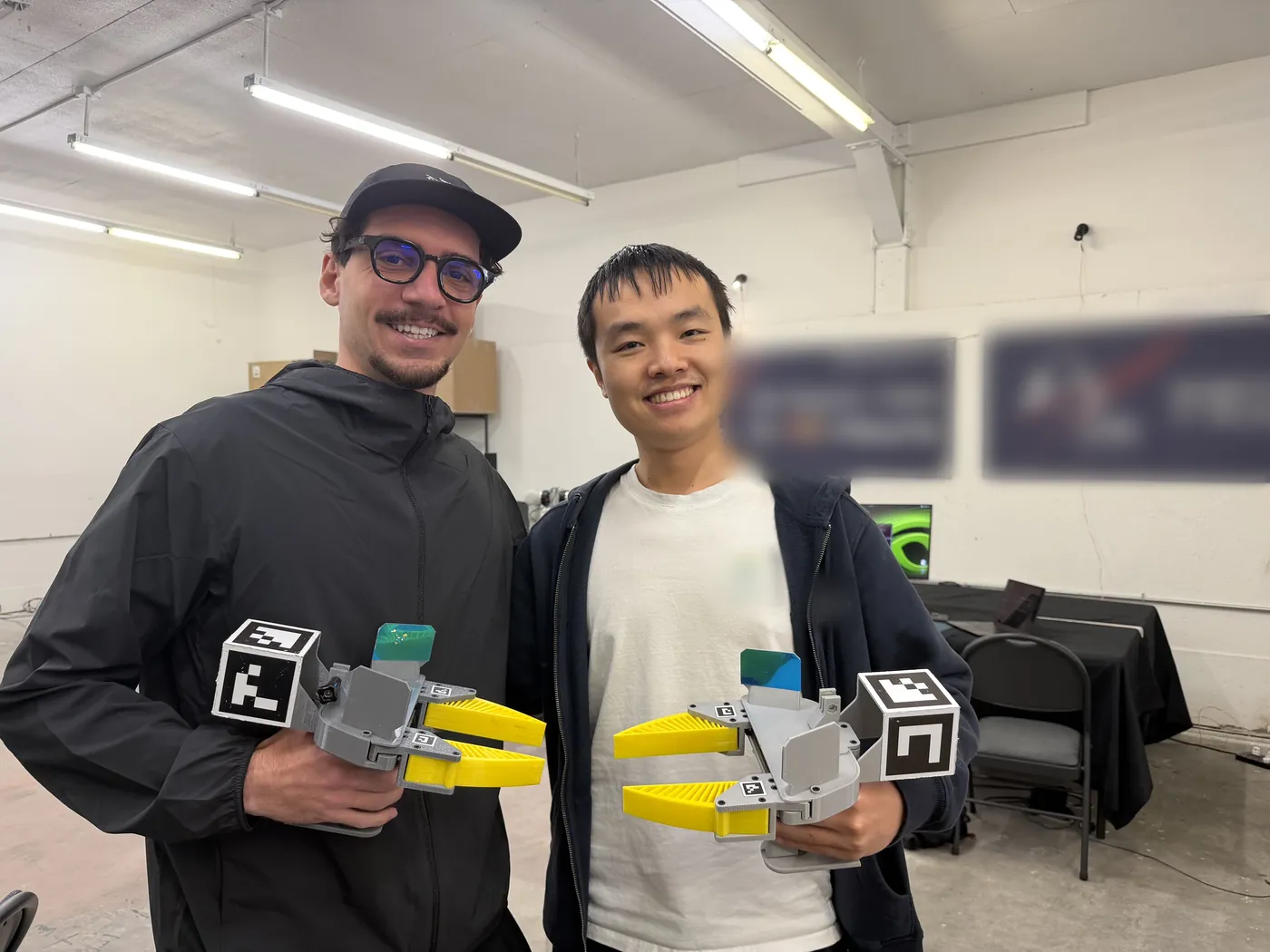 Two people holding UMI grippers at a robotics event